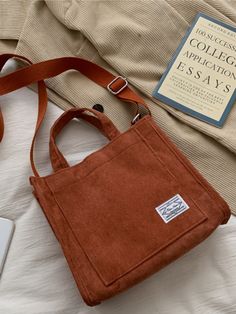 an orange bag sitting on top of a bed next to a book and a laptop