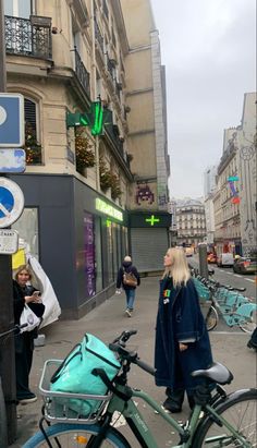 a woman standing next to a bike on a city street with other people walking by