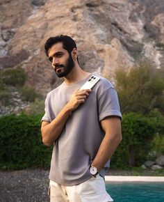 a man standing in front of a mountain with a cell phone strapped to his shoulder