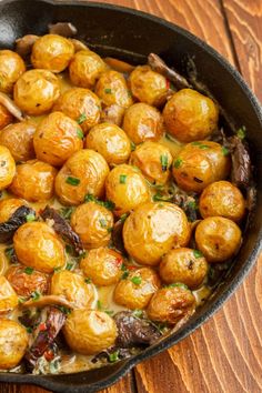 a skillet filled with cooked baby potatoes on top of a wooden table and garnished with parsley