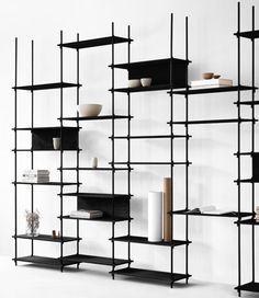 a black shelf with several shelves and vases on top of it in front of a white wall