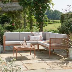 a couch and coffee table sitting on a stone patio in the middle of a garden