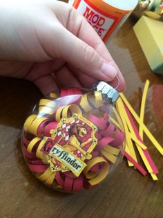 a hand is holding a small glass ornament that has been decorated with yellow and red ribbons