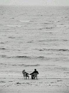 two people sitting on beach chairs facing the ocean