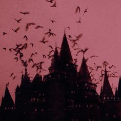 a flock of birds flying in front of a castle at dusk with pink sky behind it