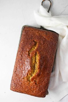 a loaf of banana bread sitting on top of a cooling rack next to a white cloth