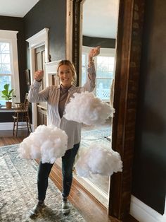 a woman standing in front of a mirror holding two fluffy clouds