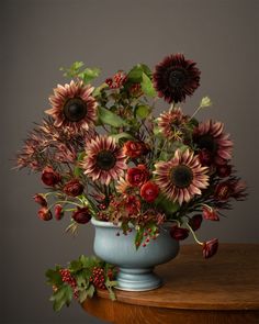 a blue vase filled with lots of flowers on top of a wooden table in front of a gray wall