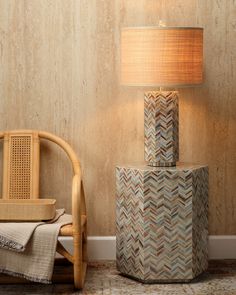 a lamp sitting on top of a wooden table next to a chair and ottoman in front of a wall