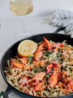 a skillet filled with pasta and shrimp next to a glass of wine