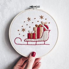 a hand is holding a small embroidery hoop with a christmas sleigh and presents on it