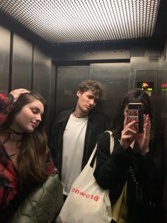 three people standing in a elevator taking pictures with their cell phones and looking at them