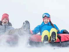 two people are sledding down a hill in the snow