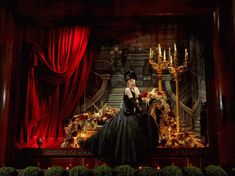 a woman in a black dress is sitting on a stage with red curtains and candles