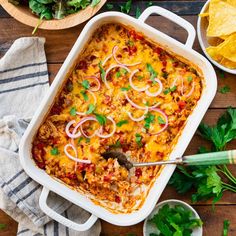 an enchilada casserole in a white dish with tortilla chips on the side