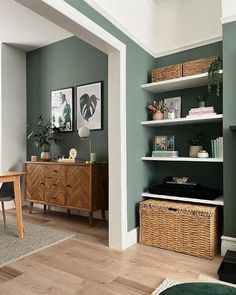 a living room with green walls and white trim on the wall, wicker baskets in front of the bookshelf