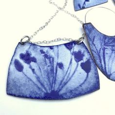 two pieces of blue glass with flowers on them are attached to silver chain necklaces