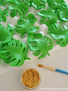 some green leaf shapes next to a paintbrush and bowl of yellow powder on a white surface