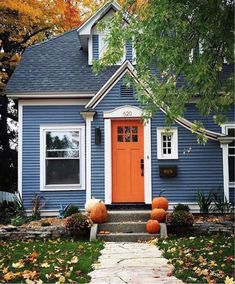 a blue house with orange front door and pumpkins on the ground in front of it