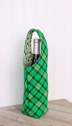 a bottle in a green and black bag on a wooden table next to a white wall