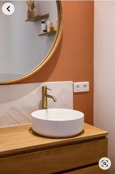 a white bowl sink sitting on top of a wooden counter next to a round mirror