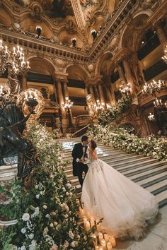 a bride and groom are standing on the stairs in an ornately decorated building with chandeliers