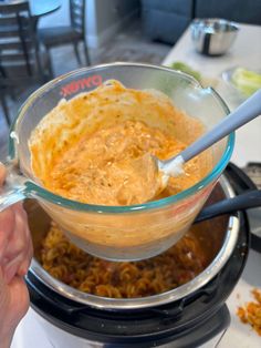 a person holding a spoon in a bowl filled with macaroni and cheese on top of a table