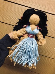 a hand holding a small stuffed doll with tassels