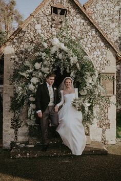 a bride and groom posing in front of an old stone building with flowers on it