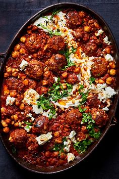 a pan filled with meatballs and cheese on top of a blue table cloth next to a fork