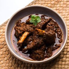 a bowl filled with meat and sauce on top of a mat next to a spoon