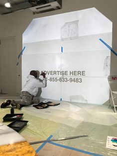 a man in white shirt and black pants painting a large sign with blue tape on it