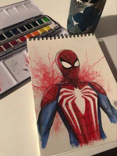 a spider man drawing on paper next to some watercolors