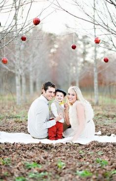 a man, woman and child are sitting on the ground in an apple orchard with apples hanging above them