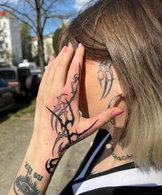 a woman with tattoos covering her face and holding her hand up to her ear while standing on the street