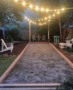 an empty backyard with string lights strung over the walkway and seating area for people to sit on