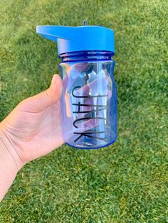 a hand holding a blue water bottle with the word think on it in front of green grass