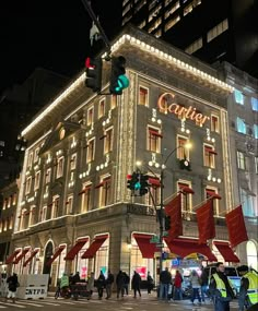 people are walking around in front of a building with lights on it at night time