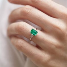 a woman's hand wearing a ring with an emerald stone in the center and diamond band