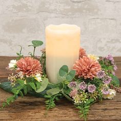 a lit candle surrounded by flowers and greenery