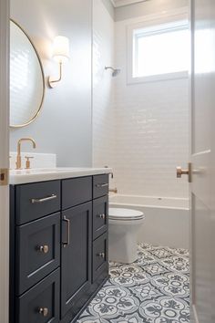 a white toilet sitting next to a bath tub under a window in a bathroom with blue and white tiles on the floor