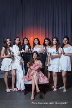 a group of women standing next to each other in front of a curtain holding wine glasses