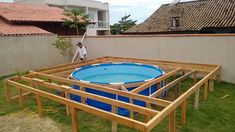 a man standing next to an above ground swimming pool in a backyard with wooden framing