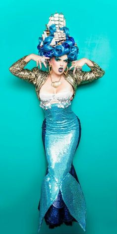 a woman with blue hair is wearing a mermaid costume and holding her hands on her head