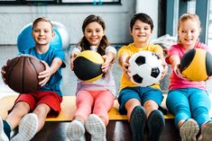 four children are sitting on the floor with balls in their hands and one child is holding a soccer ball