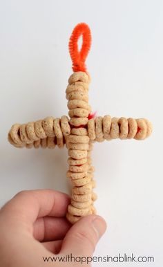 a hand holding a small cross made out of crackers with an orange ribbon on it