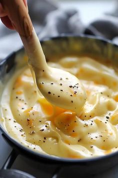 a ladle full of macaroni and cheese being lifted with a wooden spoon