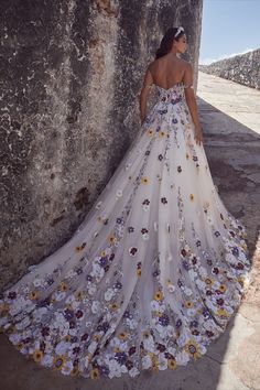 a woman standing next to a stone wall wearing a white dress with flowers on it