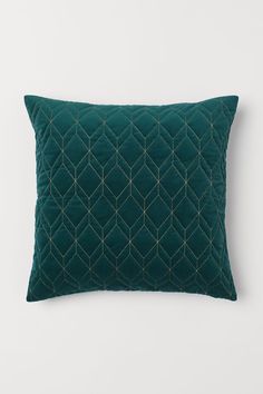 a green velvet pillow with gold threadwork on the front and back, sitting against a white wall