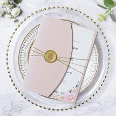 two pink wedding cards on a plate with gold trimmings and beaded edge